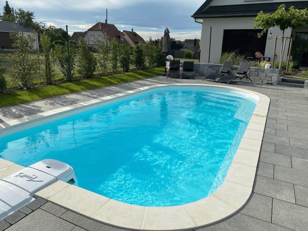 Piscine coque Axéo 570 à bloc filtrant posée par Piscine Auvergne, avec margelles et plage en dalles grises