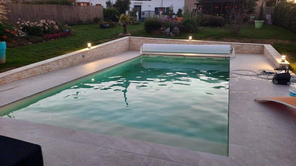 Piscine coque Réunion de 8 x 4 m avec volet roulant et murets en pierre, posée par Piscine Auvergne à Thiers